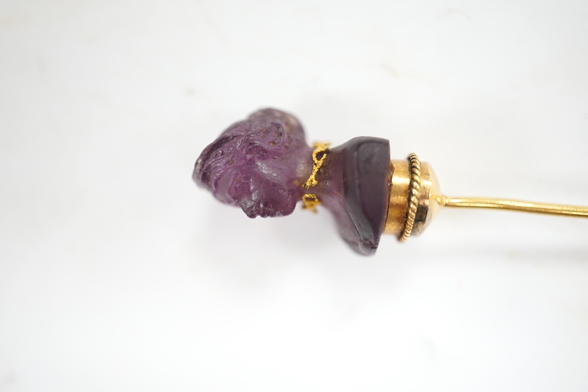 An early 20th century French yellow metal (18ct poincon mark) and amethyst paste set stick pin, the terminal modelled as the bust of a lady, 96mm, gross weight 5.6 grams. Condition - poor to fair